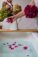 Partial view of woman throwing hydrangea petals in bath, selective focus