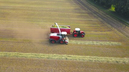 Landwirtschaftliche Erntearbeiten auf einem Feld: Feldhäcksler nimmt Grassilo auf und befördert dies auf einen Traktor mit Muldenkipper, Vogelperspektive