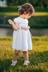 Cute, little girl in white dress looking at something in the grass.