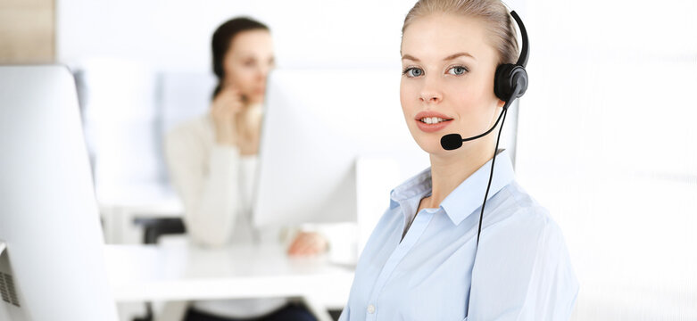 Blond woman call operator is using computer and headset for consulting clients online. Group of diverse people working as customer service occupation. Business concept