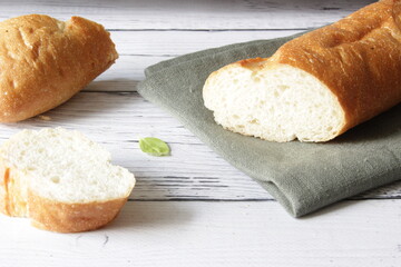 Naklejka premium French fresh soft bread baguette on napkin and wooden background. Several cut pieces are lying next to each other.