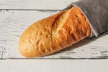 French fresh soft bread baguette on napkin and wooden background. Several cut pieces are lying next to each other.