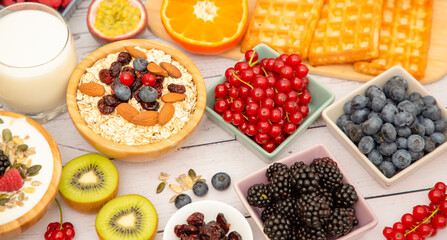 Breakfast Served in the morning with Butter bread and corn flakes Whole grains and raisins with milk in cups and Strawberry, Blueberry, Raspberry, Kiwi, Fresh Orange  on the breakfast table.