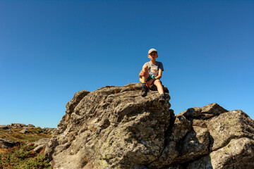 boy sitting on the edge of a large rocky rock, summer hike in the mountains, the top of the mountain.