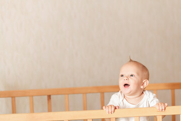 baby boy stands in the crib in the bedroom and laughs