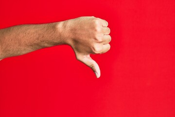 Arm of caucasian white young man over red isolated background doing thumbs down rejection gesture,...
