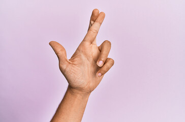 Arm and hand of caucasian young man over pink isolated background gesturing fingers crossed, superstition and lucky gesture, lucky and hope expression