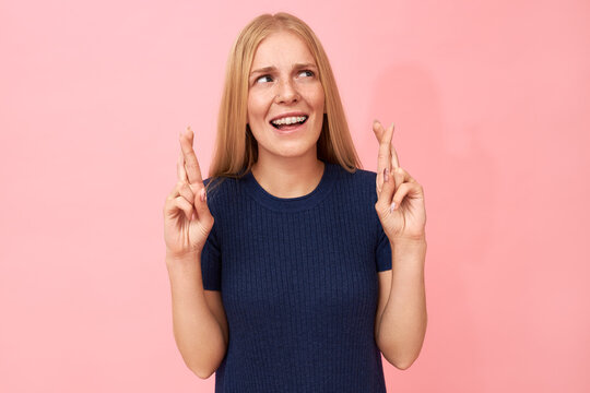 Isolated image of superstitious young woman with teeth braces looking up making hand gesture to protect herself against bad luck or evil, wishing for favor, hoping all her dreams come true
