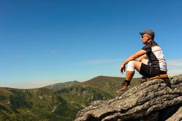 traveler, tourist, traveler stands on top of a cliff and enjoys a sunny day and a view of the picturesque Carpathians.
