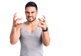 Fototapeta premium Young handsome man wearing swimwear and sleeveless t-shirt shouting frustrated with rage, hands trying to strangle, yelling mad