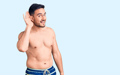 Fototapeta premium Young handsome man wearing swimwear smiling with hand over ear listening an hearing to rumor or gossip. deafness concept.