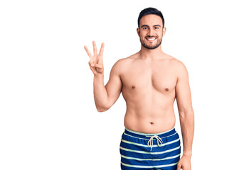Young handsome man wearing swimwear showing and pointing up with fingers number three while smiling confident and happy.