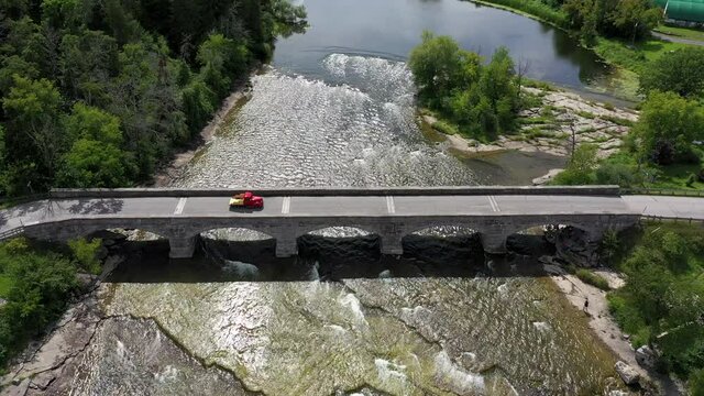 vintage red truck crosses stone bridge high wide aerial showing rapids