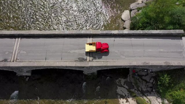 red vintage pickup truck crossing stone arch bridge above view following
