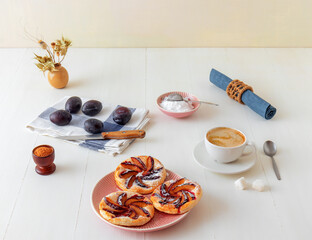 Small plum tarts on plate with cinnamon and icing sugar on white wooden table, delicious puff pastry dessert.