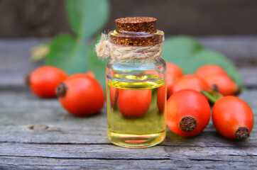 Rosehip essential oil in a glass bottle with rose hips berries on old wooden table for skin care or spa.Selective focus.
