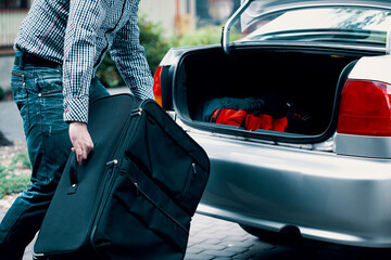 Man holding big suitcase in front of open car trunk
