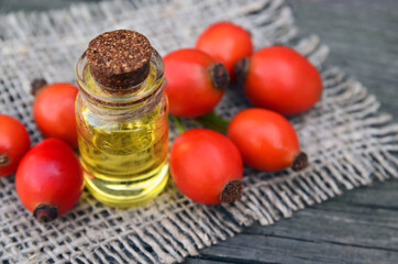 Rosehip essential oil in a glass bottle with rose hips berries on old wooden table for skin care or spa.Selective focus.