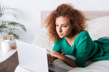 Selective focus of red haired woman using laptop on bed