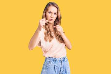 Young beautiful caucasian woman with blond hair wearing casual clothes ready to fight with fist defense gesture, angry and upset face, afraid of problem