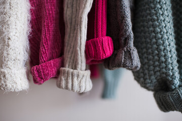Knitted clothes with folded sleeves hang on hanger indoors closeup. Winter season.
