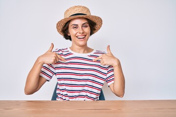 Young hispanic woman wearing casual clothes and hat sitting on the table looking confident with...