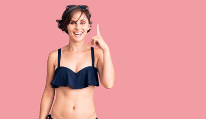 Obraz premium Beautiful young woman with short hair wearing bikini pointing finger up with successful idea. exited and happy. number one.