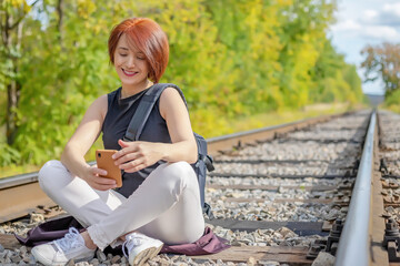 happy pretty red-haired young woman sitting on the railroad track with phone in her hands