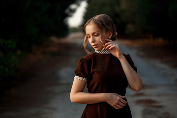 close-up portrait of a young beautiful girl in a brown dress in a retro style on an abandoned road