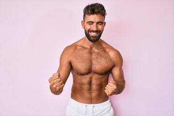 Fototapeta premium Young hispanic man standing shirtless very happy and excited doing winner gesture with arms raised, smiling and screaming for success. celebration concept.