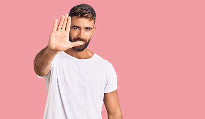 Fototapeta premium Young hispanic man wearing casual white tshirt doing stop sing with palm of the hand. warning expression with negative and serious gesture on the face.