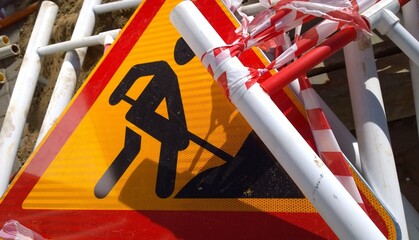 Road works sign denoting construction work and metal fencing on the ground. Close up. Red and...