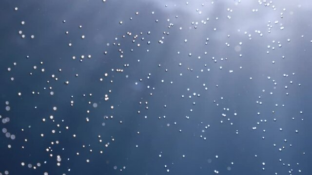 air bubbles underwater in blue water moving strange some in focus some out of focus making nive background shapes with sun rays and sun shine