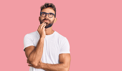 Young hispanic man wearing casual clothes and glasses with hand on chin thinking about question, pensive expression. smiling and thoughtful face. doubt concept.