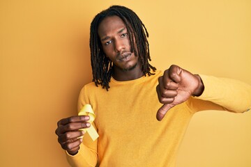 African american man with braids holding suicide prevention yellow ribbon with angry face, negative...