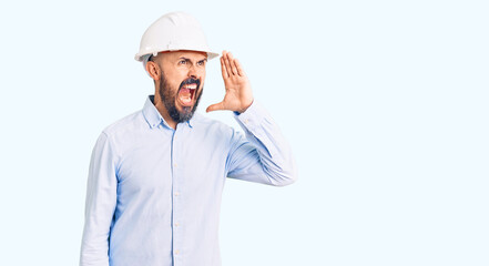 Young handsome man wearing architect hardhat shouting and screaming loud to side with hand on mouth. communication concept.
