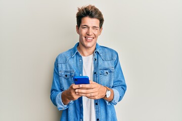 Handsome caucasian man using smartphone winking looking at the camera with sexy expression,...