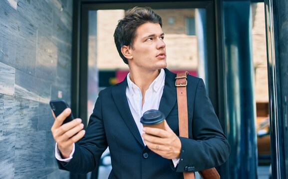 Young caucasian businessman with serious expression using smartphone and drinking coffee at the city.