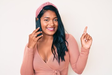 Beautiful latin young woman with long hair having conversation talking on the smartphone smiling happy pointing with hand and finger to the side