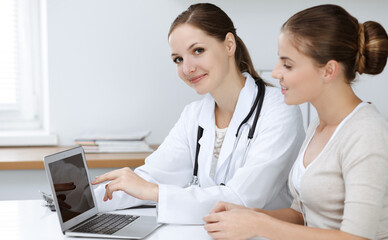 Doctor and patient sitting and discussing health examination results while using laptop computer. Health care, medicine and good news concepts