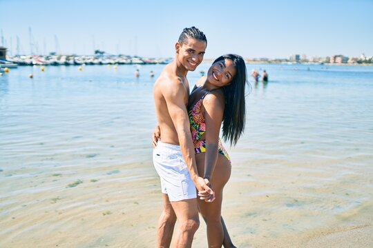 Young latin couple wearing swimwear  smiling happy and dancing at the beach.