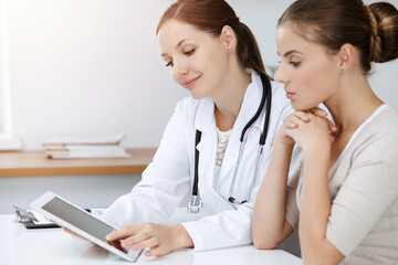Doctor and patient are sitting and discussing health examination results while using tablet computer
