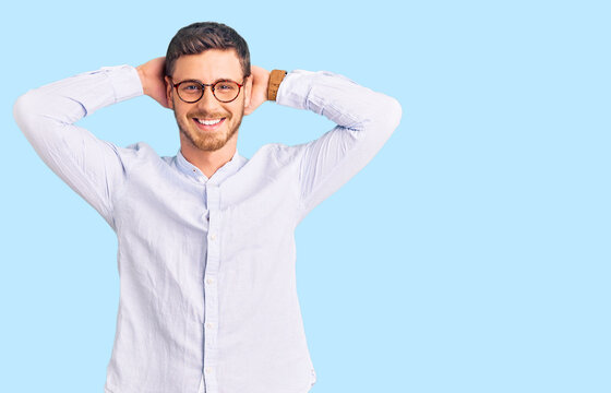 Handsome young man with bear wearing elegant business shirt and glasses relaxing and stretching, arms and hands behind head and neck smiling happy
