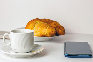 Morning breakfast: a cup of coffee, croissants, newspaper and mobile phone on the table