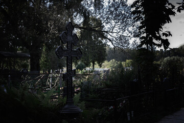 Black grave cross in the cemetery, dusk nightfall night. Gloomy scary photo at dusk, old metal...