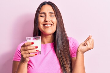 Young beautiful brunette woman drinking glass of milk screaming proud, celebrating victory and success very excited with raised arm