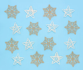 Gold snowflakes and white wooden stars on pastel blue background. Christmas pattern for packaging. New year minimal concept. Top view, flat lay