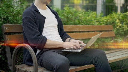 Young guy working in park sitting on bench with laptop, no face. Sitting in the park at summer day...