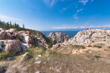 Cape Sagan-Khushun or Rocks Three brothers with red moss on the background of blue water and blue sky in summer time. Olkhon Island on Lake Baikal. Eastern Siberia, Russia