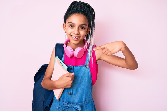 Young african american girl child with braids holding student backpack and books pointing finger to one self smiling happy and proud